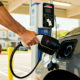 An EV owner preparing to plug a Level 2 charging connector into his electric car at a public charging station.