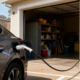 Electric car charging outside a home garage on a sunny day using a Level 2 EV charger