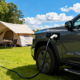 A pickup truck camping on the grassland, using a portable EV charger to power camping gear outdoors.